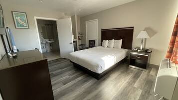 A hotel room with a large bed, bedside tables, a desk, a mirror, and a bathroom visible through an open door.