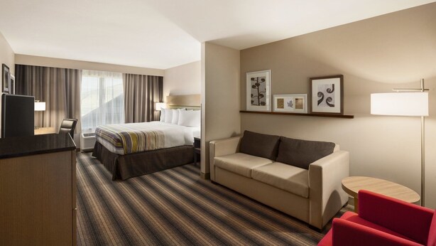 A hotel room with a bed, a sofa, a desk, and a red chair. - Country Inn & Suites by Radisson, Sandusky South, OH (Milan)