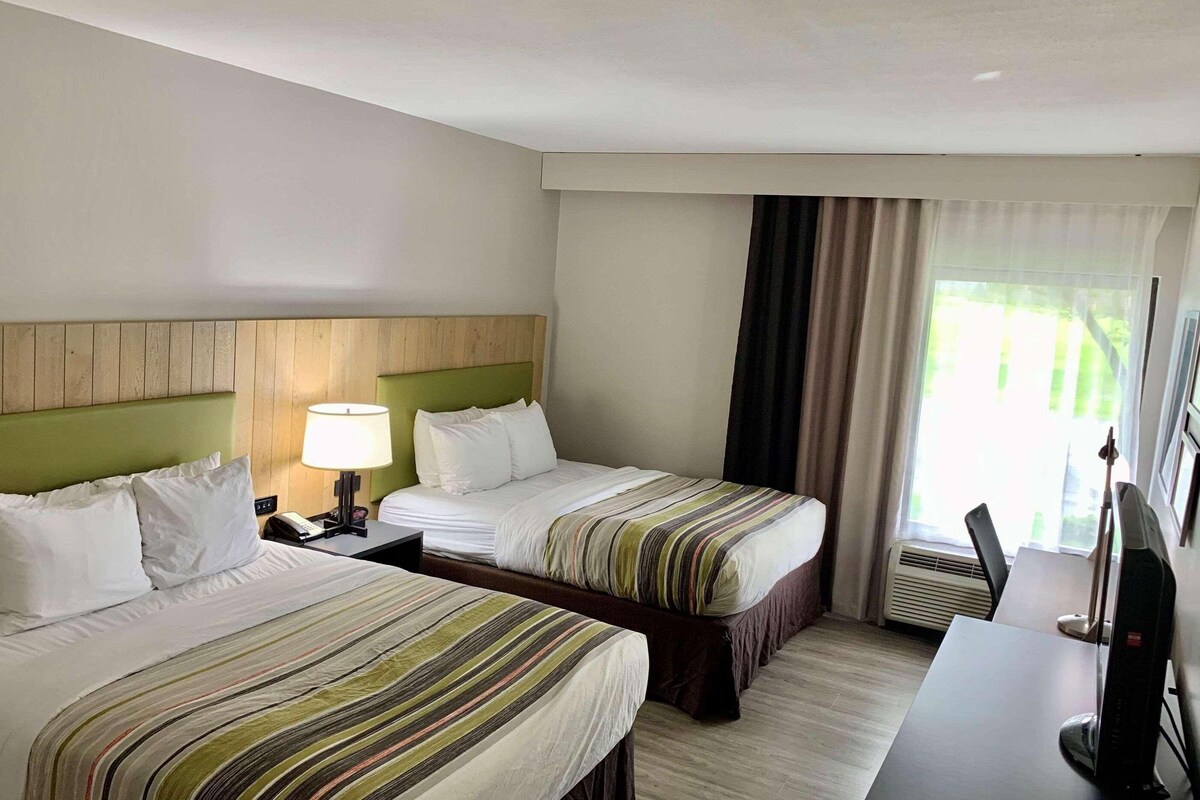 A hotel room with two beds, a desk, a lamp, and a TV.