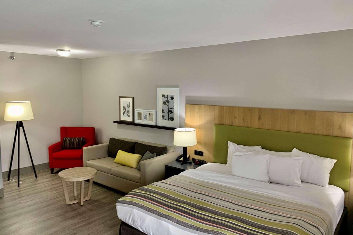 A hotel room with a bed, a sofa, a red armchair, a small round table, and two floor lamps.