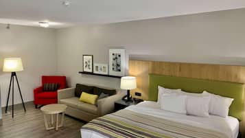 A hotel room with a bed, a sofa, a red armchair, a small round table, and two floor lamps.