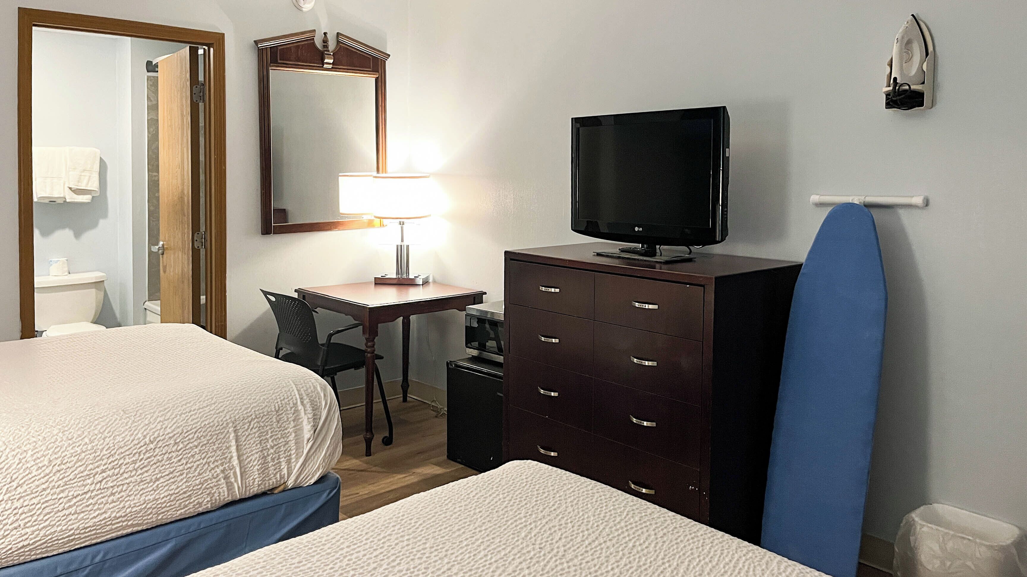 A hotel room with two beds, a desk with a lamp, a dresser, a television, and a mirror.