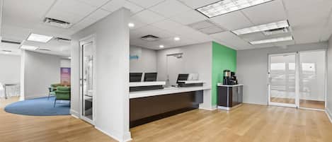 A modern office space with a reception desk, a coffee station, and a green accent wall.