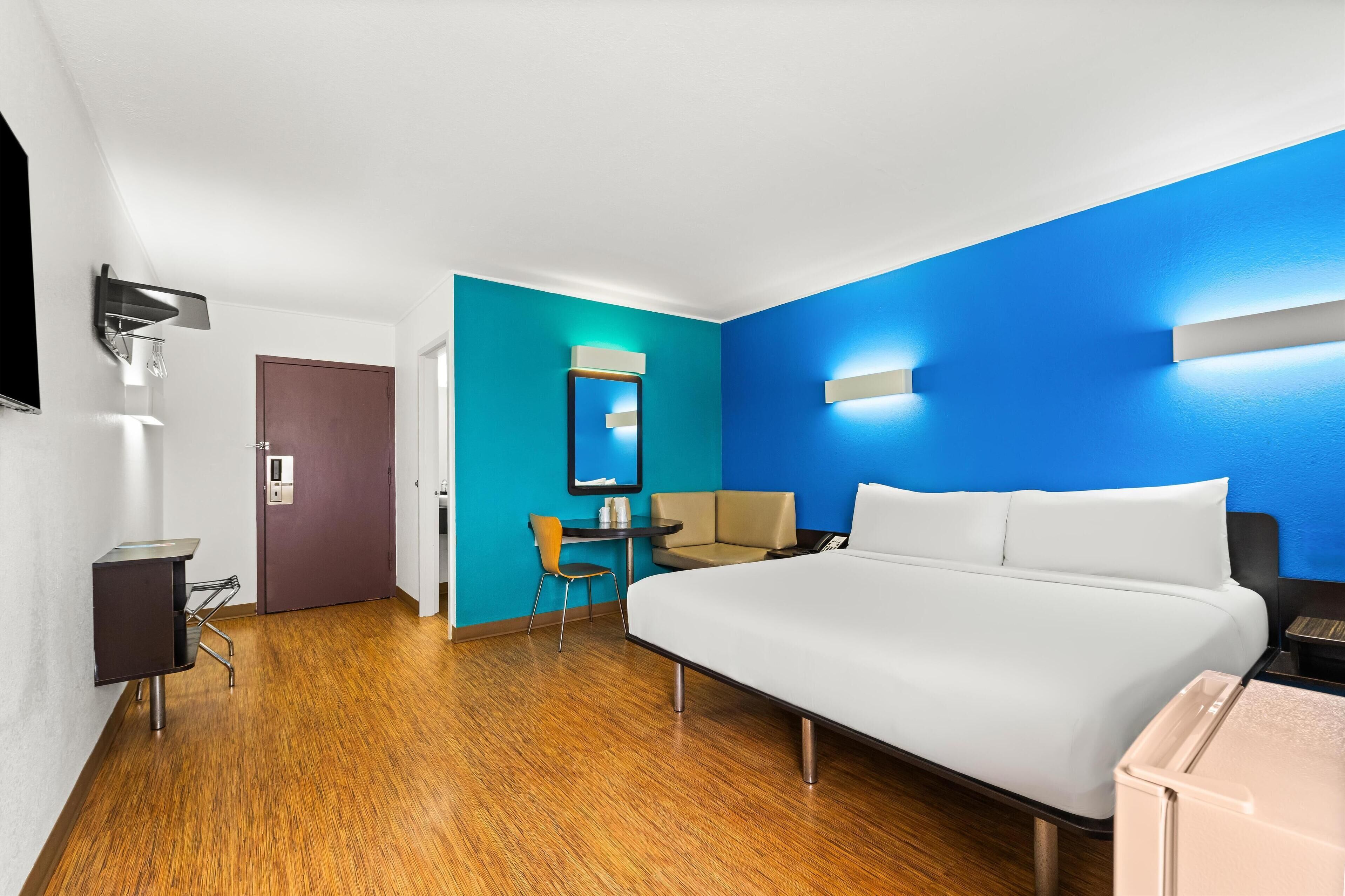 Une chambre d’hôtel avec un grand lit, un bureau, une chaise, un miroir et un téléviseur.