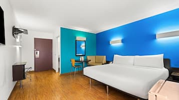 A hotel room with a large bed, a desk, a chair, a mirror, and a TV.