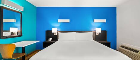 Una habitación de hotel moderna con una cama grande, un escritorio y una silla. Hay dos mesitas de noche con lámparas y un espejo en la pared.