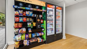Una máquina expendedora de aperitivos con papas fritas y otros bocadillos, y un refrigerador con bebidas.