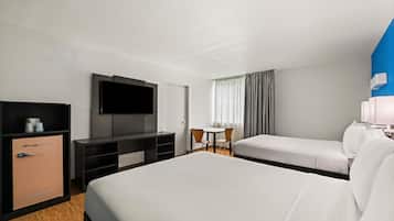 A hotel room with a bed, a TV, a minibar, a desk, and a window with curtains.
