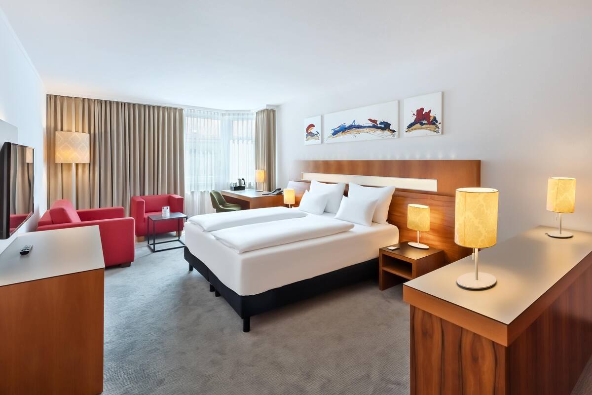 A hotel room with a large bed, a desk, a chair, and a TV.