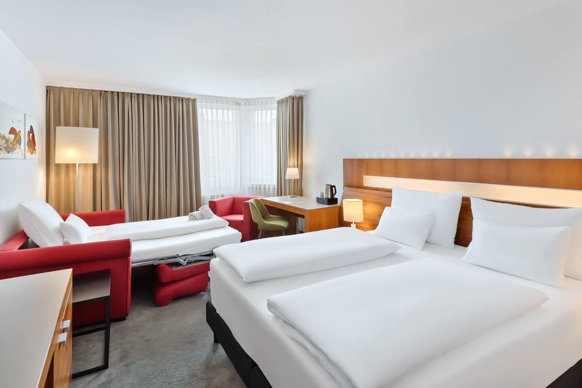 A hotel room with two beds, a desk, a chair, and a sofa.