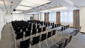 A conference room with rows of black chairs, a projector screen, and large windows with curtains.