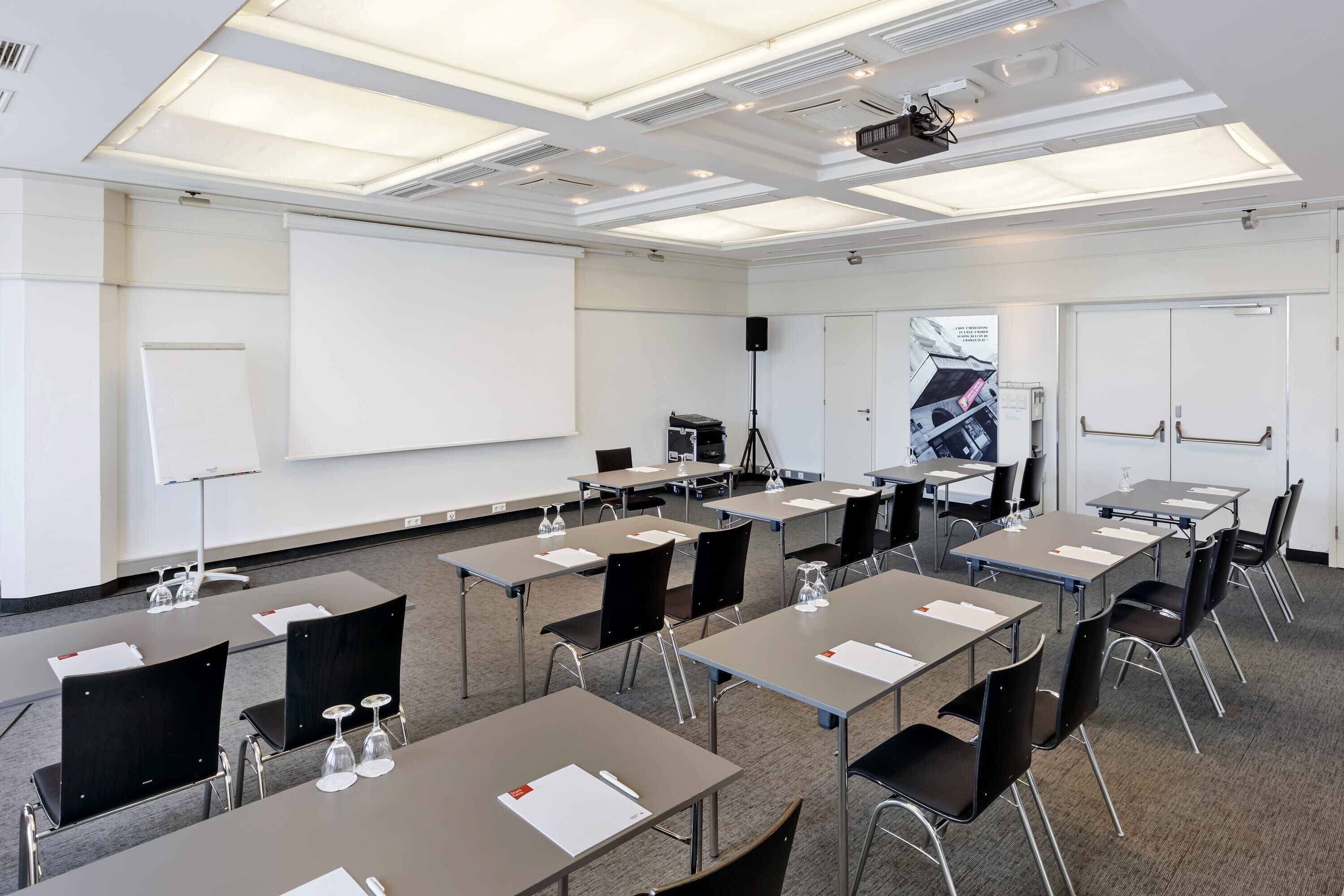 Un salón de conferencias con varias mesas, sillas, un proyector y una pizarra.