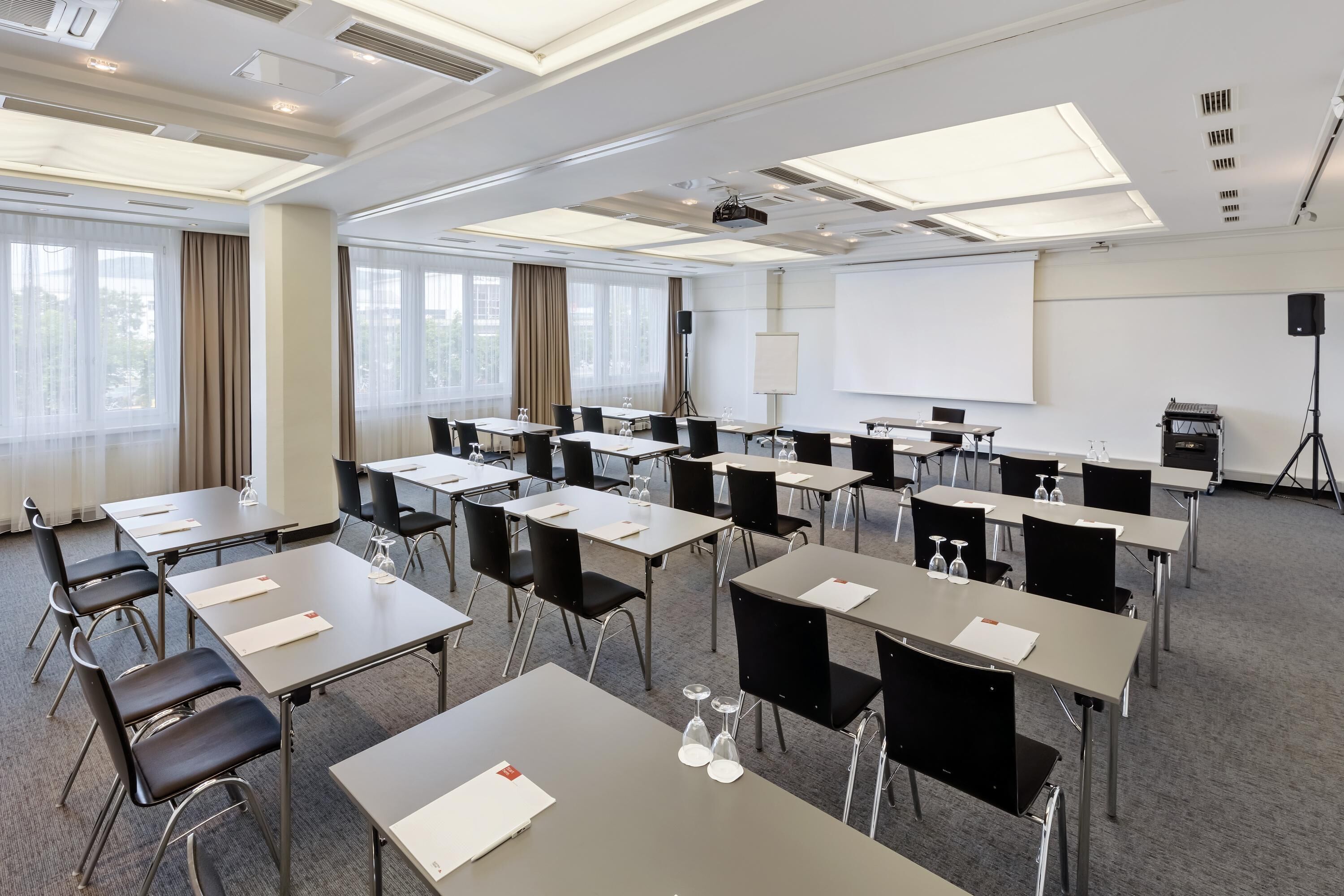 Uma sala de conferências com várias mesas, cadeiras, um projetor e um quadro branco.