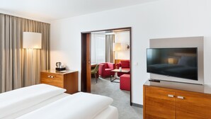A hotel room with a bed, a TV, a desk, and a seating area with a red sofa and chairs. - Austria Trend Hotel Europa Graz Hauptbahnhof (Graz)