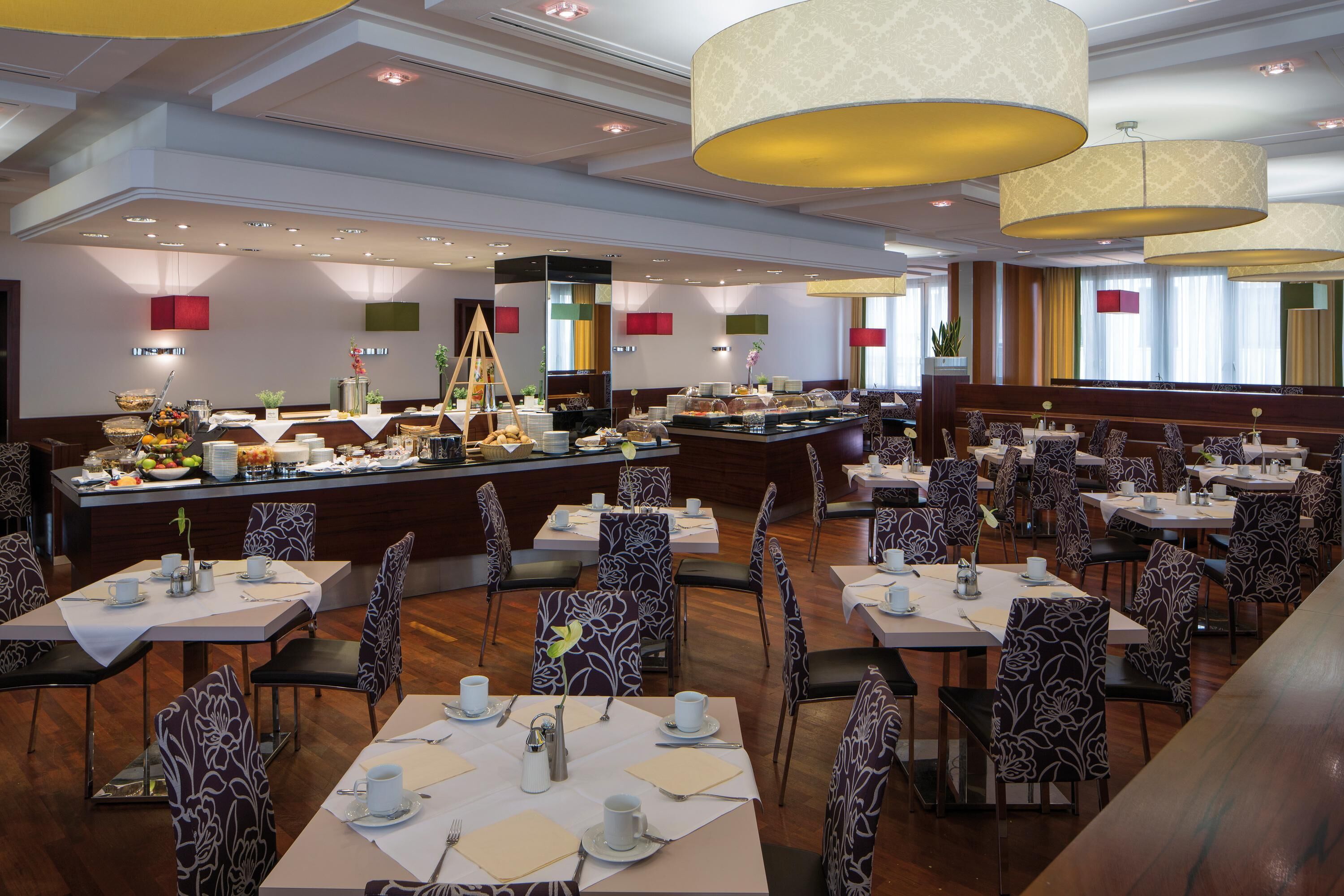 A hotel dining area with multiple tables and chairs, a buffet counter, and pendant lighting.