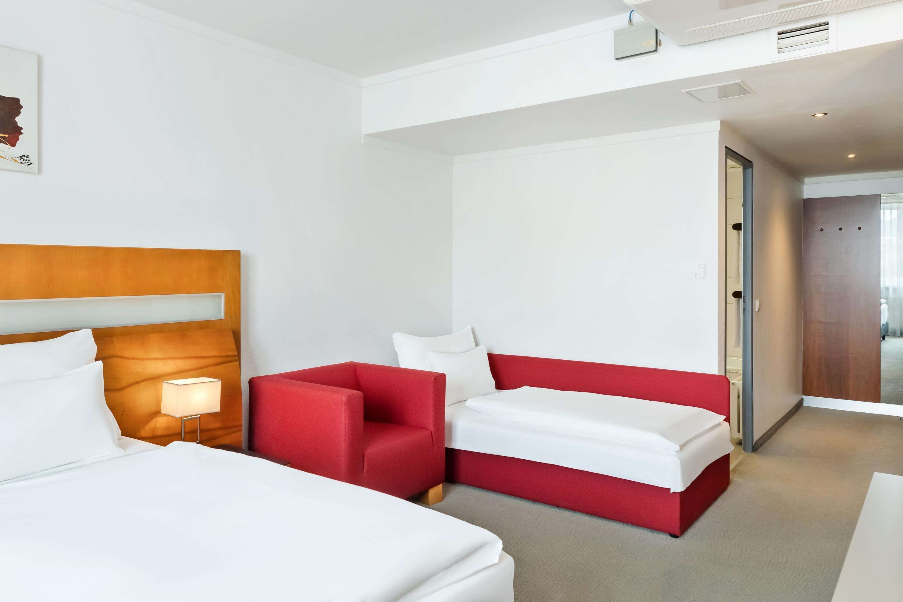 Una habitación de hotel con una cama grande, un sillón rojo y un sofá más pequeño.