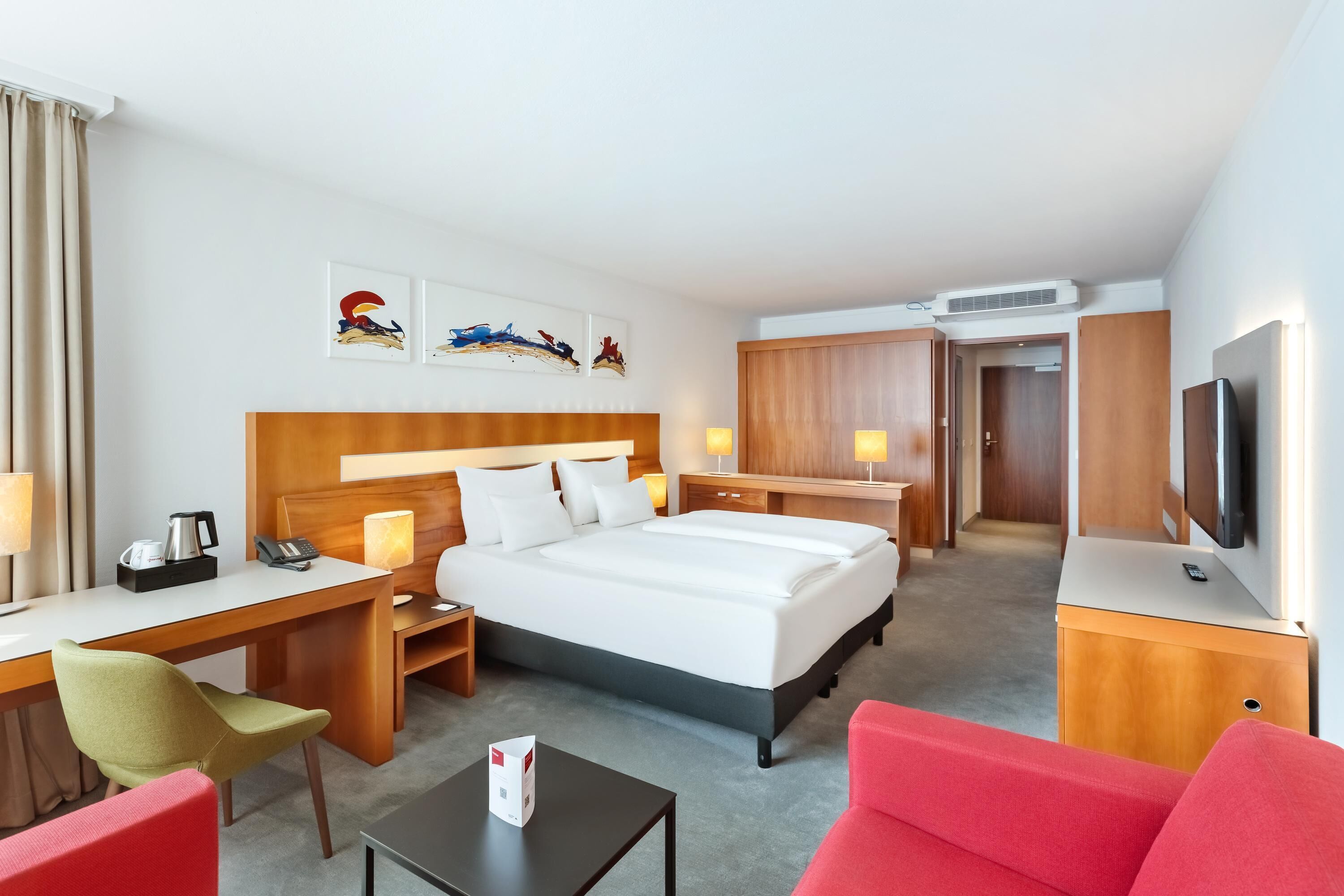 Een hotelkamer met een groot bed, een bureau met stoel, een televisie en kunst aan de muur.