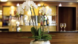 A bar area with a vase of white orchids, two glasses of white wine, and a wooden counter. - Austria Trend Hotel Europa Graz Hauptbahnhof (Graz)