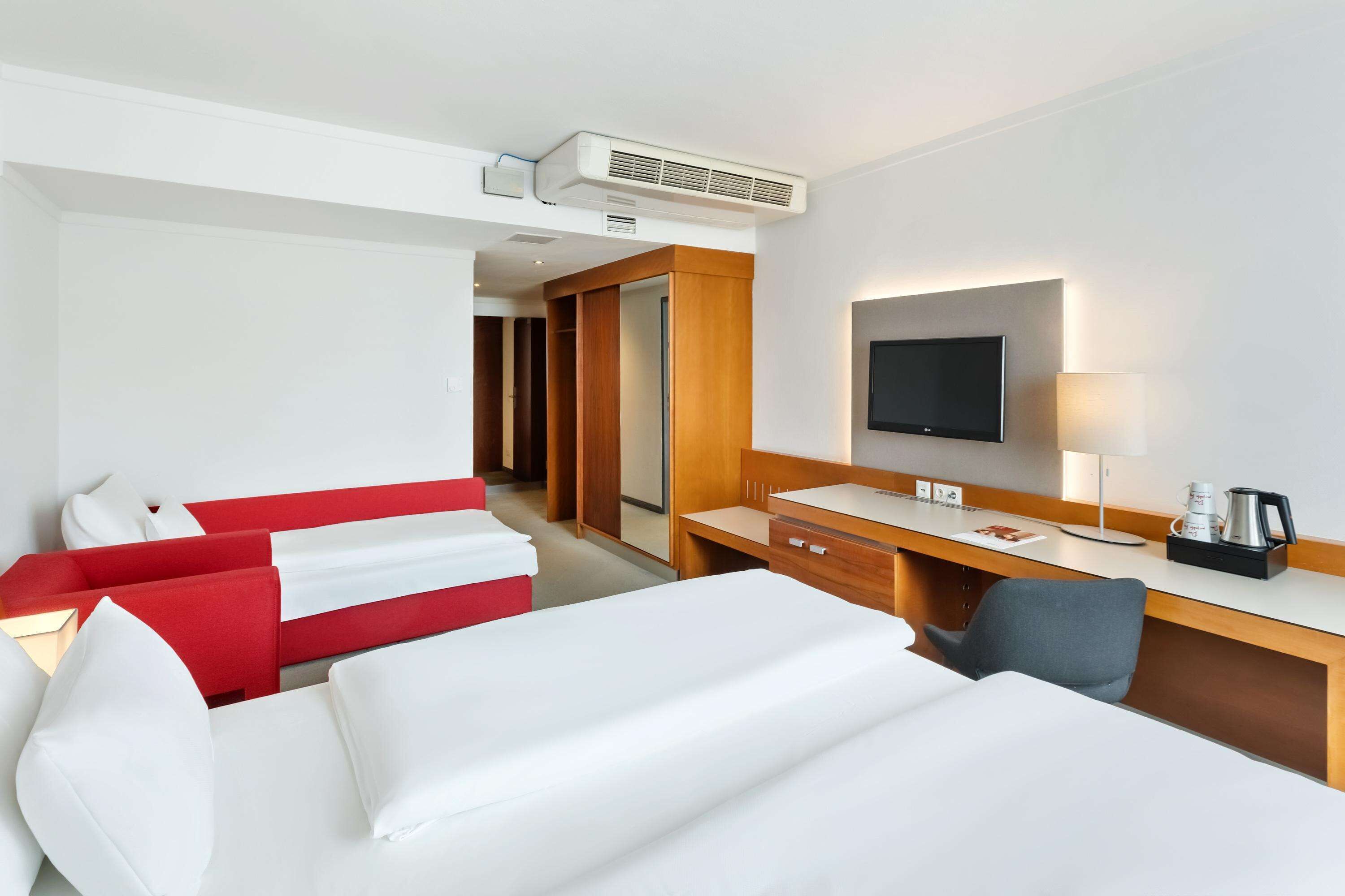A hotel room with a bed, a desk with a flat-screen TV, a coffee maker, and a wardrobe.