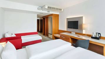 A hotel room with a bed, a desk with a flat-screen TV, a coffee maker, and a wardrobe.