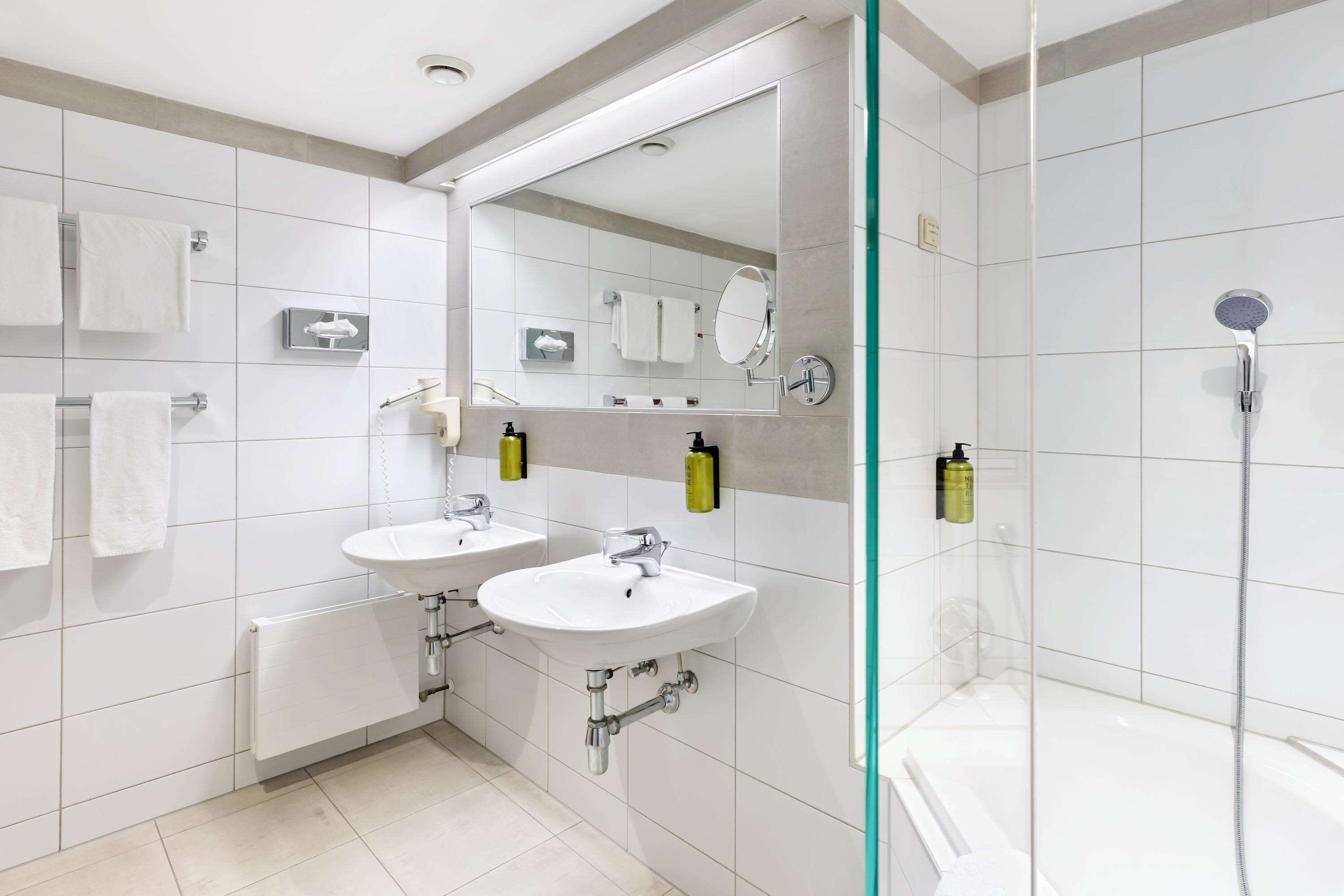A modern bathroom with two sinks, a large mirror, and a glass-enclosed shower.
