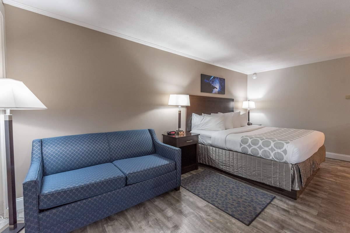 Une chambre d’hôtel avec un canapé bleu, un lit recouvert d’une couvre-lit à motifs, deux lampes de chevet et une petite table de nuit avec une horloge.