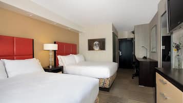 A hotel room with two beds, a desk, a chair, a lamp, and a television.