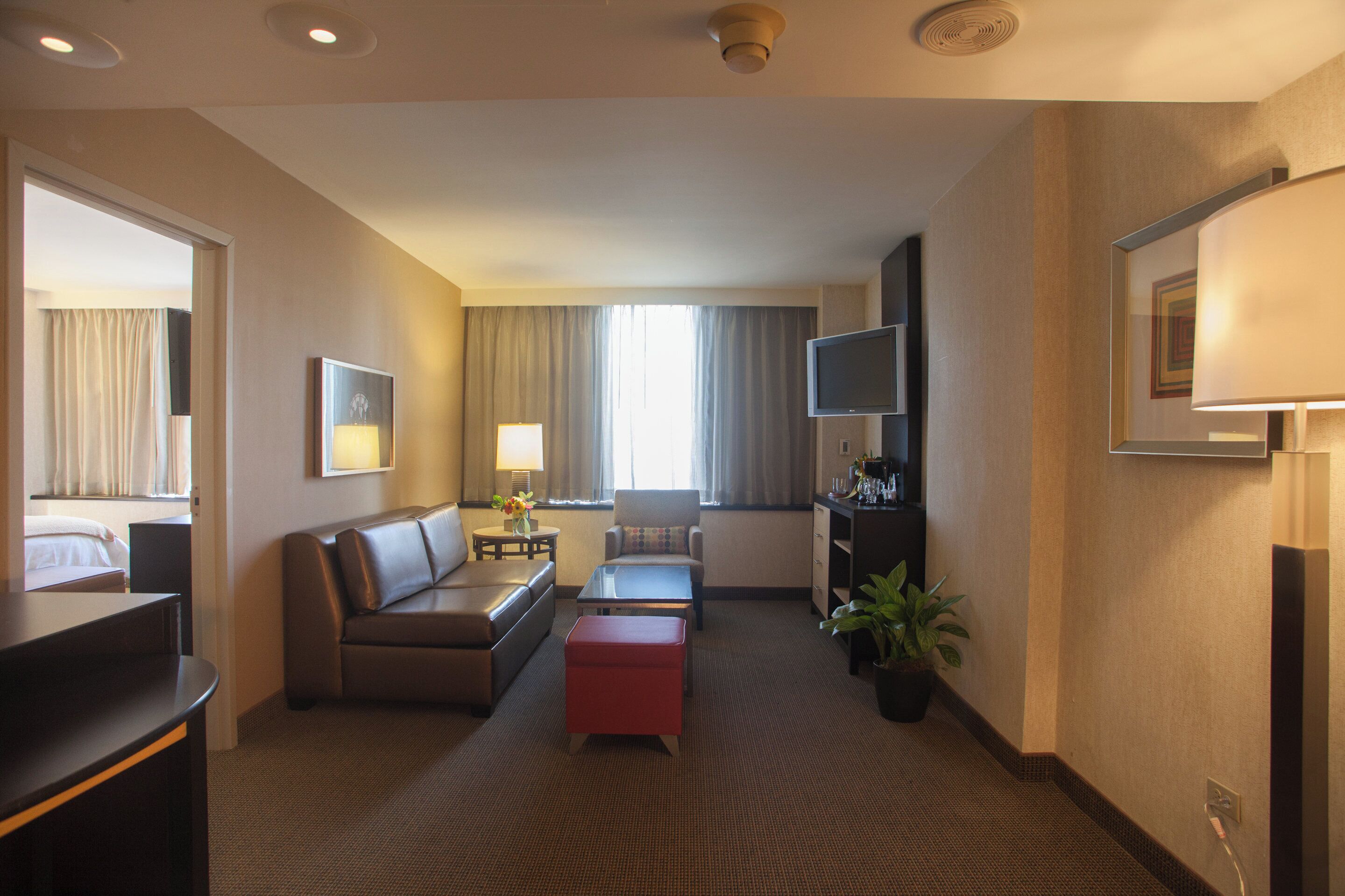 A hotel room with a sofa, a small table, a TV, and a window with curtains.