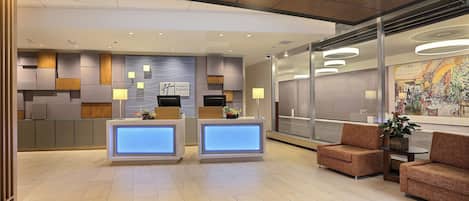 A hotel lobby with a reception desk, seating area, and a large window with a view.