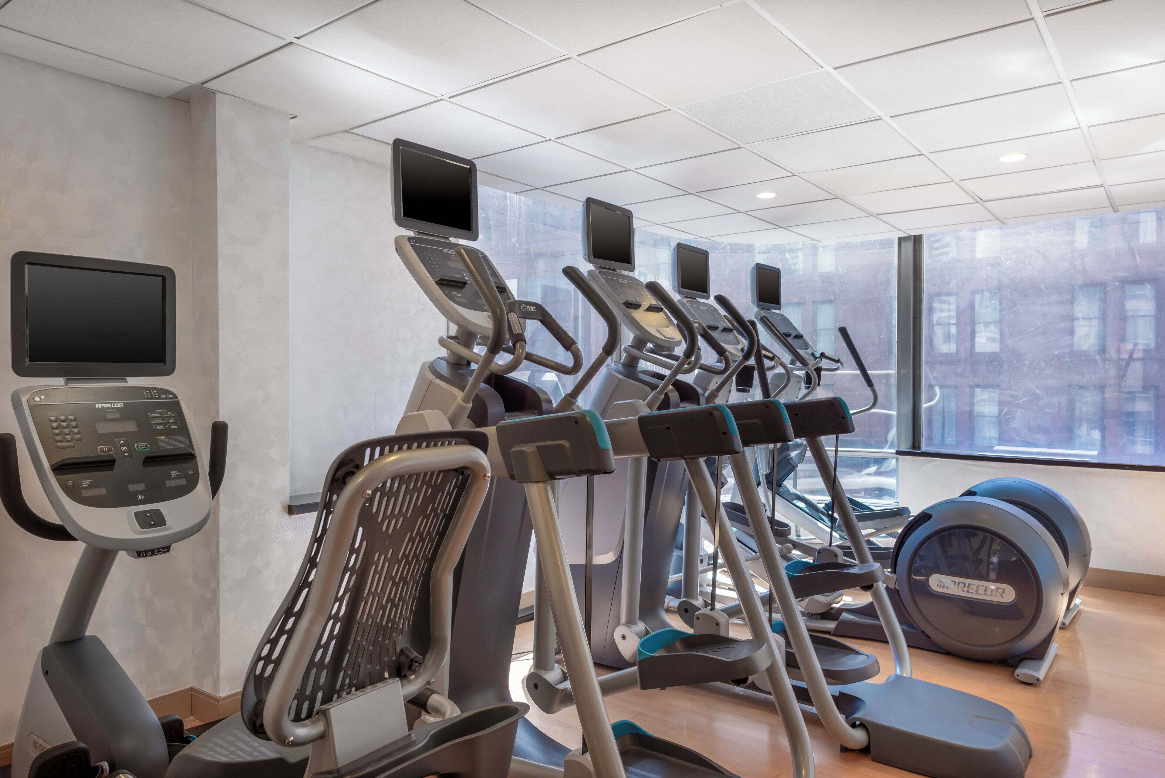 A gym with multiple treadmills, ellipticals, and a stationary bike, equipped with digital screens and a control panel.