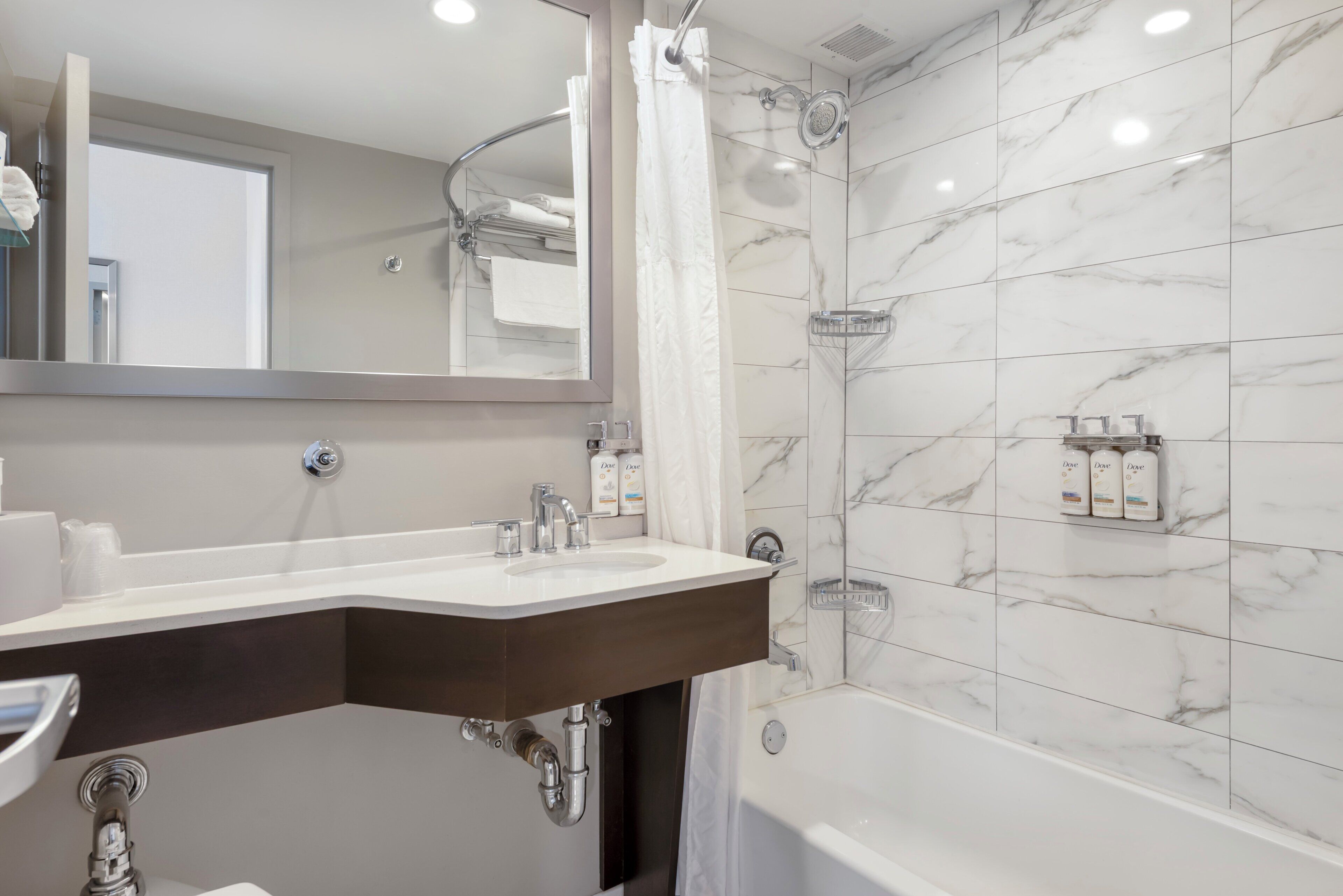 Un baño moderno con ducha revestida de mármol, un espejo grande y un tocador con lavabo y toallero.