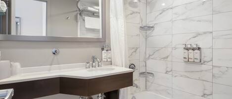 Un baño moderno con ducha revestida de mármol, un espejo grande y un tocador con lavabo y toallero.