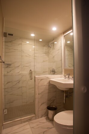 A bathroom with a glass-enclosed shower, a sink with a mirror, and a toilet.