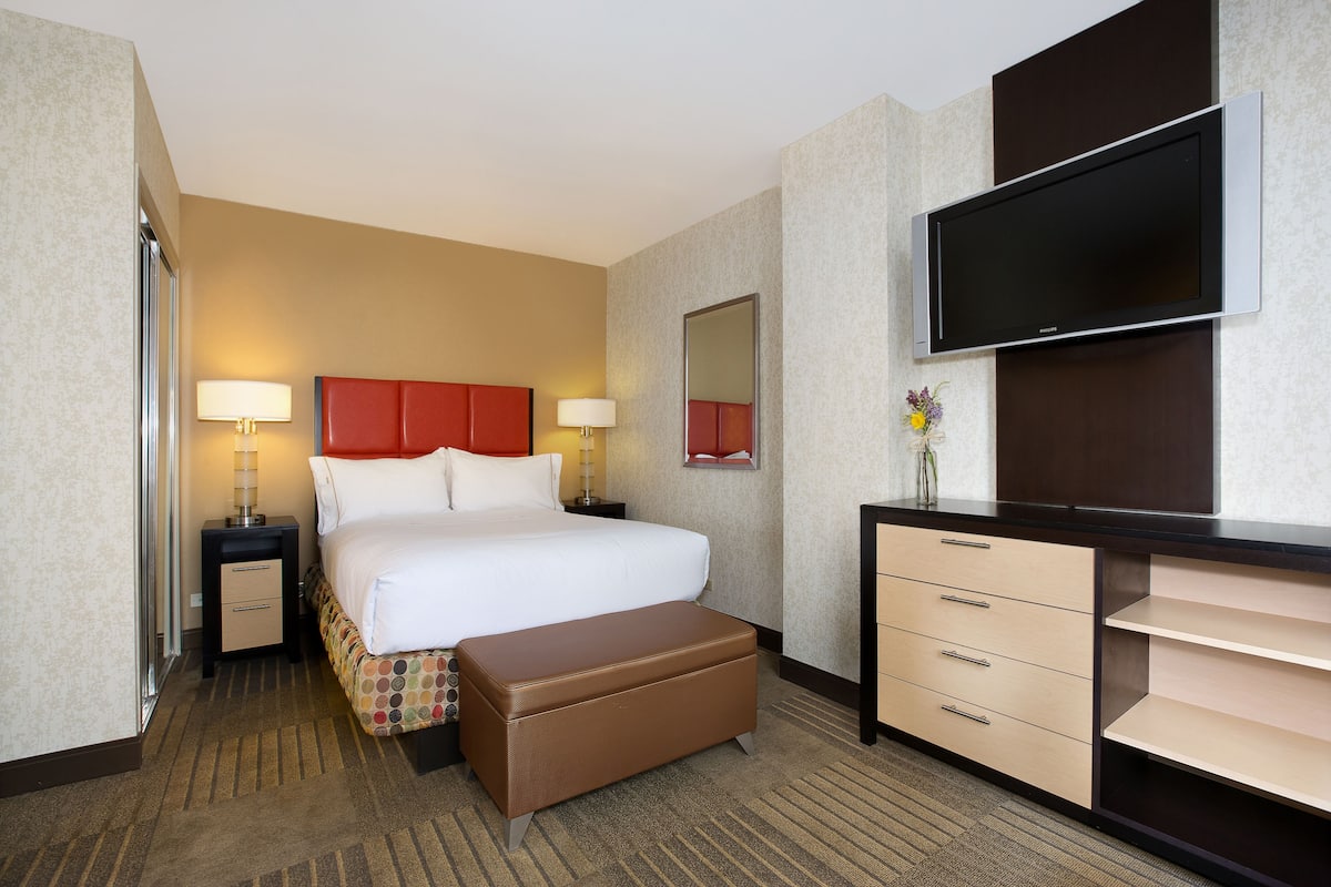 A hotel room with a bed, bedside tables, a TV, a dresser, and a mirror.
