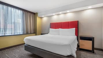 A hotel room with a large bed, a nightstand, a window with curtains, and a modern ceiling design.