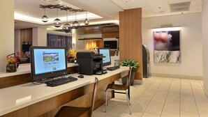 A reception desk with two monitors, a printer, and a keyboard. There is a chair in front of the desk, and a plant to the right.