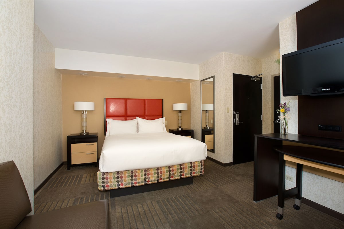 A hotel room with a bed, two bedside tables, a desk, a TV, and a mirror.