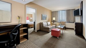 A hotel room with a desk, a sofa, a TV, and a window with curtains.