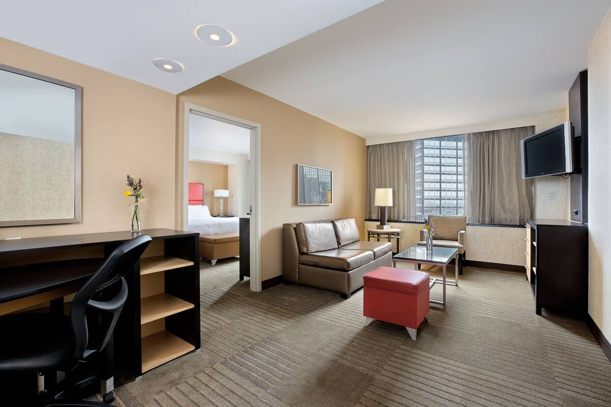 A hotel room with a desk, a sofa, a TV, and a window with curtains.