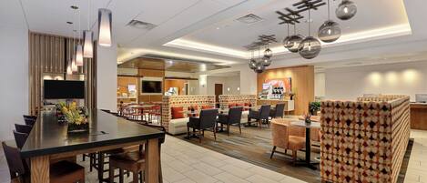 A modern hotel lobby with a dining area, seating arrangements, and a reception desk.