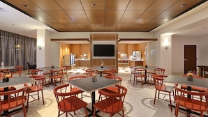 A spacious conference room with multiple tables and chairs, a large flat-screen TV, and a wooden ceiling.