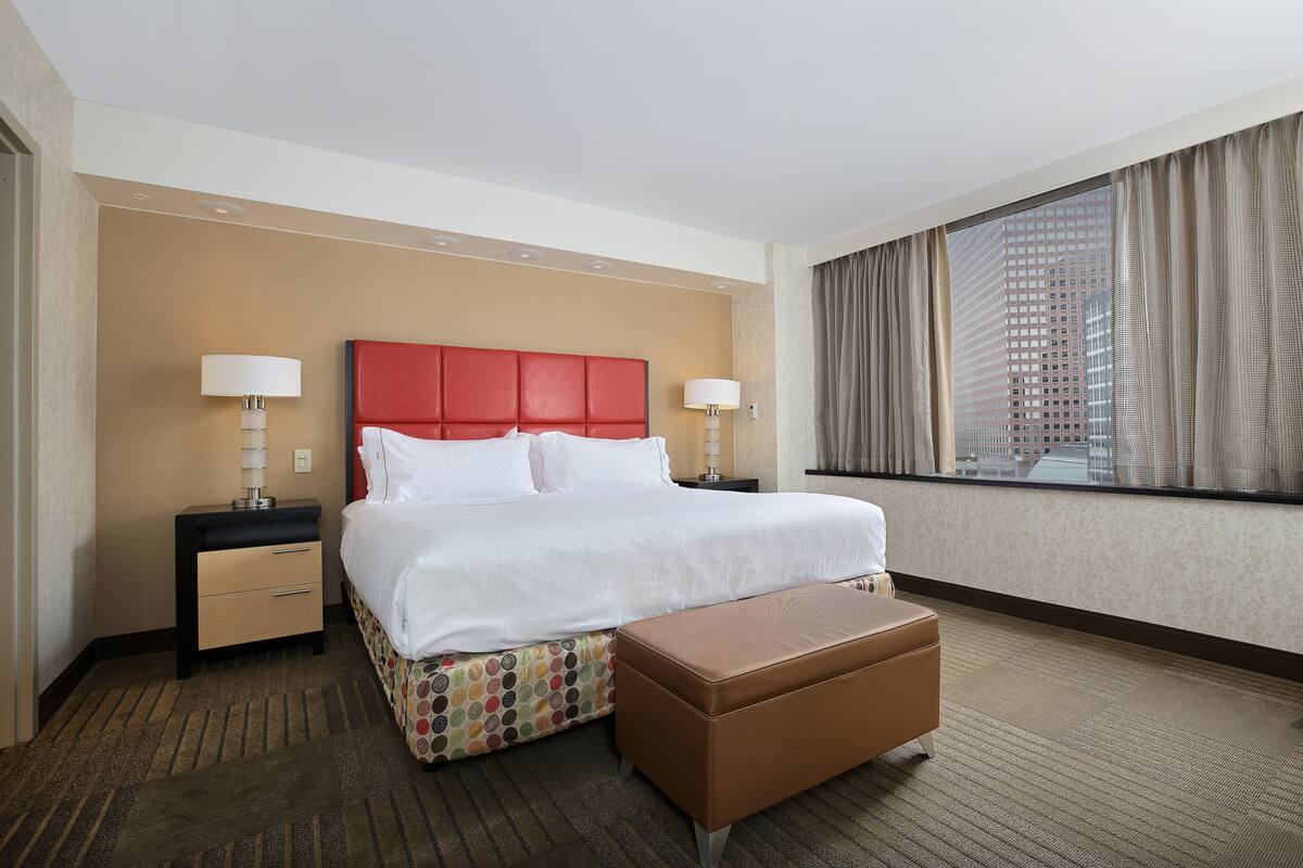 A hotel room with a large bed, two bedside tables, a window with curtains, and a view of a building.