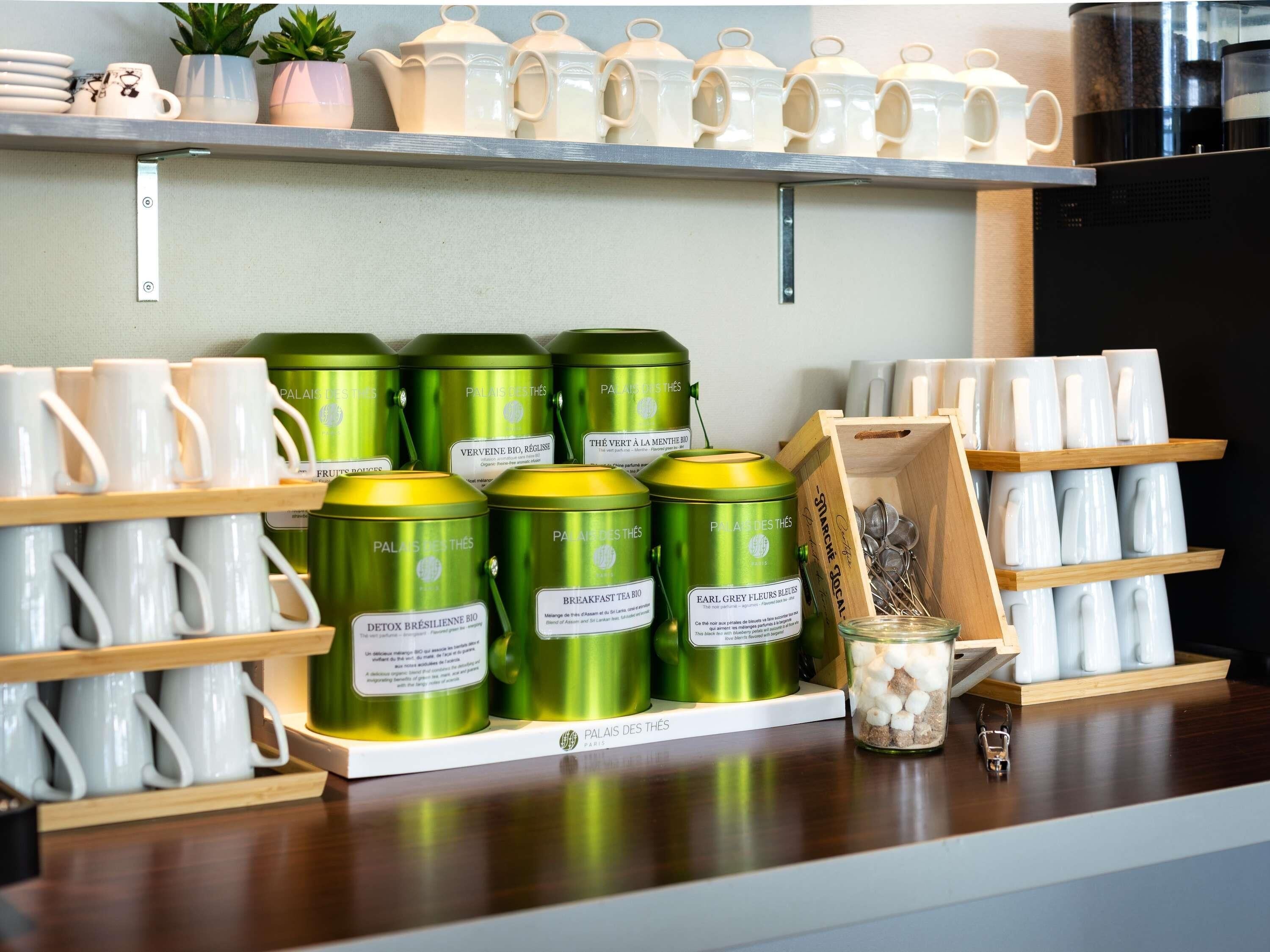 A kitchen counter with tea and coffee mugs, green tea cans, and a jar of marshmallows.