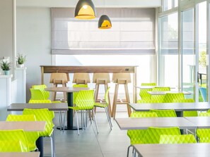 Un espace de restauration moderne, doté de tables et de chaises, de grandes fenêtres et de luminaires suspendus.