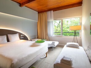 Une chambre d’hôtel avec deux lits, une table de chevet, une lampe et une fenêtre donnant sur un paysage verdoyant.