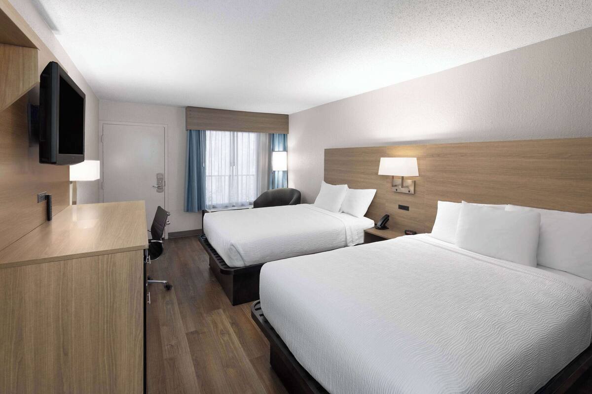 Ein Hotelzimmer mit zwei Betten, einem Schreibtisch, einem Fernseher und einem Fenster mit Vorhängen.