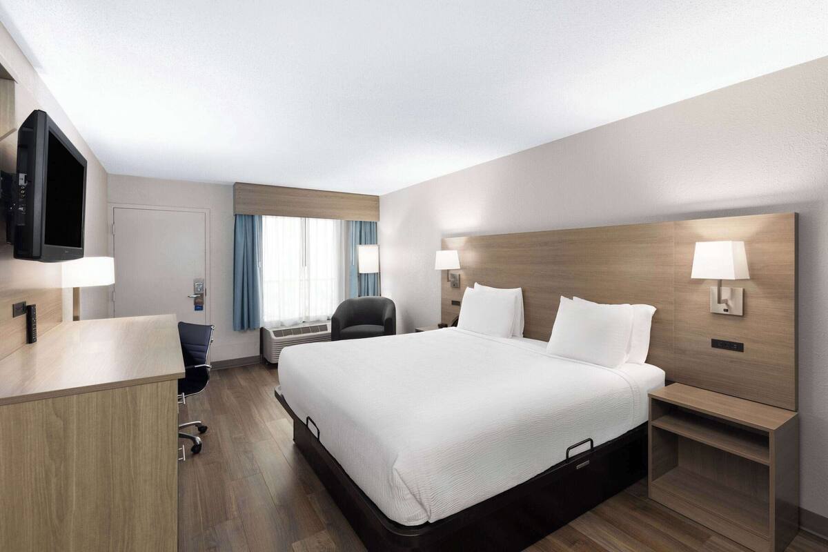 Ein Hotelzimmer mit einem großen Bett, einem Schreibtisch, einem Sessel, einem Fernseher und zwei Nachttischlampen.