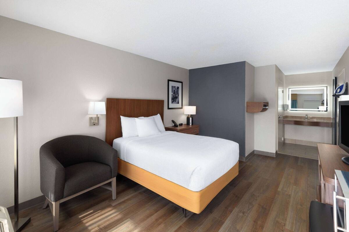 Ein Hotelzimmer mit Bett, Stuhl, Schreibtisch, Spiegel und einer kleinen Küchenzeile.