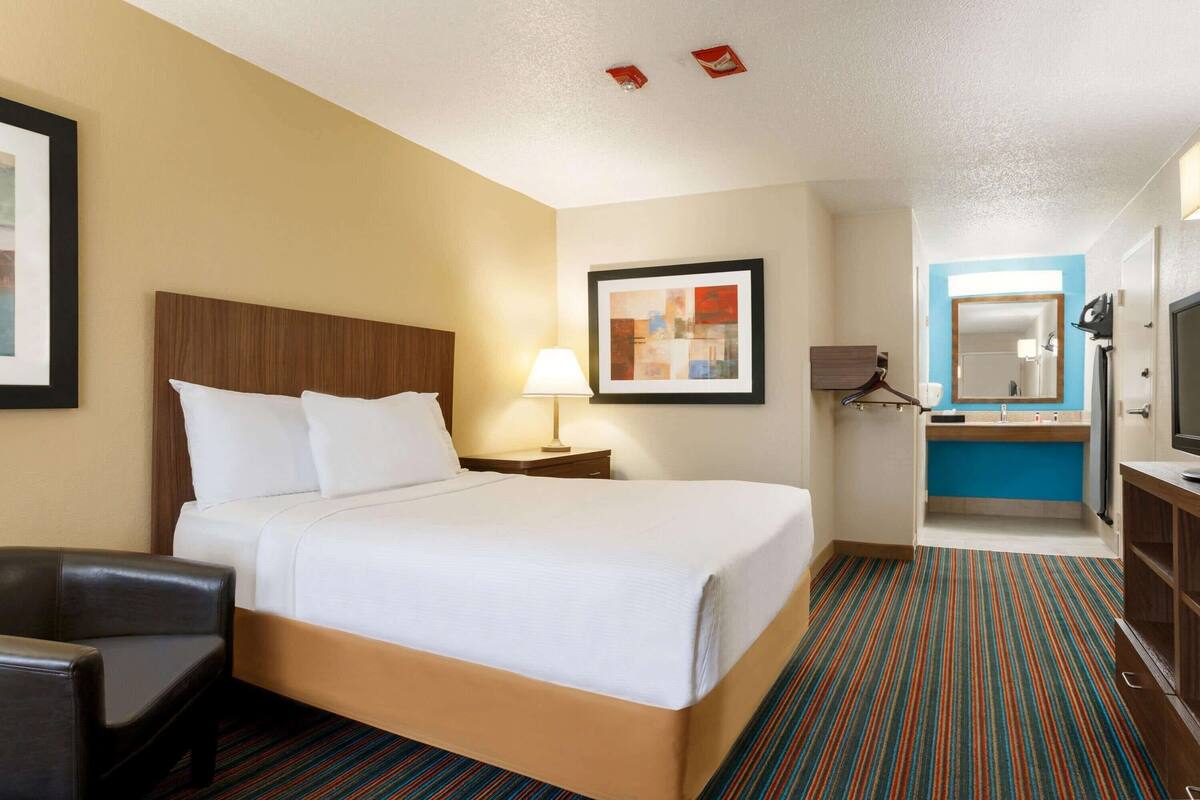 Ein Hotelzimmer mit Bett, Schreibtisch, Stuhl sowie einem Badezimmer mit Spiegel und Fernseher.