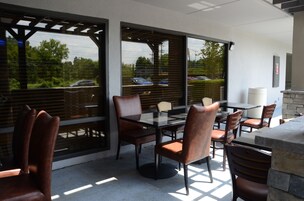 An outdoor patio with a glass table and chairs, surrounded by large windows and a stone wall.